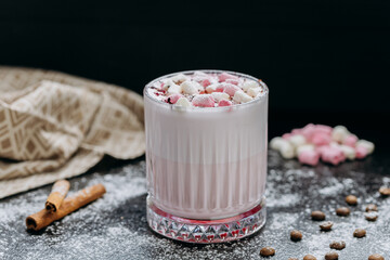 Cup of pink hot chocolate with marshmallows and powdered sugar on a rustic dark background