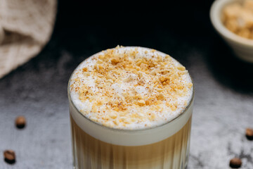 Layered latte with frothy milk and crushed nuts in crystal glass with coffee beans on dark table