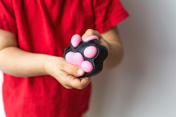 A child in a red T-shirt squeezes a black and taba pink paw-shaped squishy toy, engaging in sensory and stress-relief play
