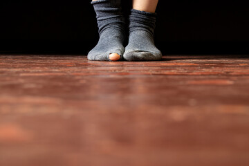Women's legs with a torn sock on the floor of a house in poverty and dirt, torn sock