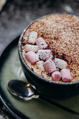 Cup of hot chocolate with marshmallows and cocoa powder on a rustic dark background