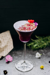 Elegant purple cocktail in a martini glass, garnished with dried lime, petals, and edible flowers