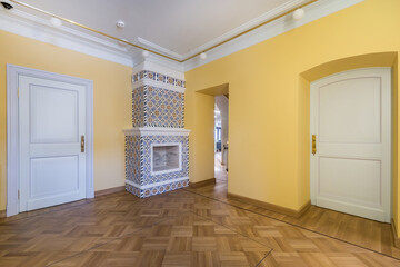 An empty room with white doors and yellow walls. Fireplace decorated with colorful tiles.