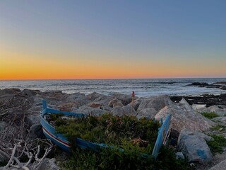 Abandoned boast on a stony beach. Sunset beyond the sea. 