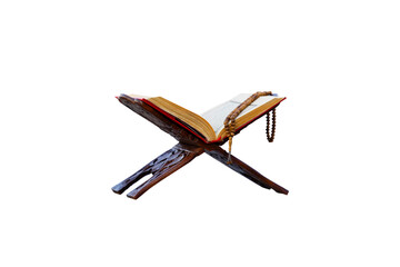 A close-up shot of an open Quran on a traditional wooden stand  with a string of prayer beads laid...