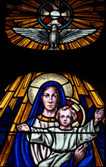 Fototapeta premium Stained glass (19th century) of Blessed Virgin Mary holding baby Jesus Christ in her arms with the Holy Spirit.