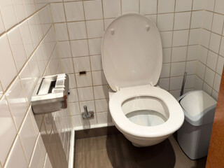 Clean white toilet in tiled bathroom with open lid next to waste bin