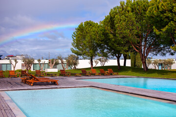 Swimming pool with sun loungers and a rainbow in the sky