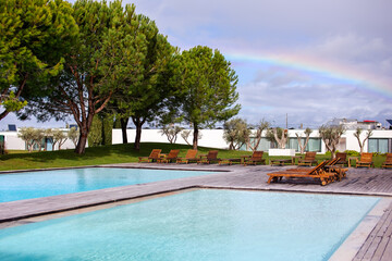 Swimming pool with sun loungers and a rainbow in the sky