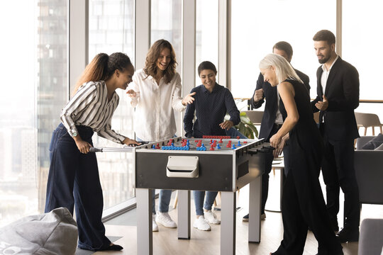 Group of happy multiethnic colleagues playing foosball, fighting table soccer, having fun, enjoying office leisure during lunch break. Friendship and recreational activity at workplace, stress relief