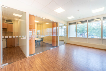 Bright Office Space With Glass Partitions and Modern Wooden Flooring. A spacious and bright office interior with glass walls, wooden flooring, and natural sunlight filtering through large windows,