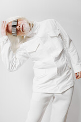 Futuristic fashion model with reflective visor and white outfit striking a pose against a plain...