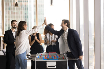 Group of happy workmates play football tabletop game in office at lunch break, giving high five, celebrate success, enjoy result and fair competition completion. Fun at workplace, friendship, unity