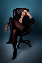 Elegant young woman in black jacket posing confidently in chair against blue gradient background