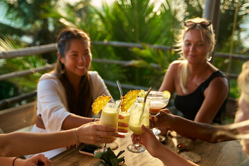 Diverse group of women at tropical restaurant toast with cocktails. Celebration. Vacation mood. Fun...