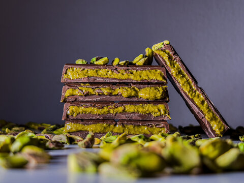 Viral and trending! Luxury Dubai chocolate stacked elegantly, with one row leaning, surrounded by vibrant green pistachios. A perfect shot for gourmet, luxury, and oriental sweets