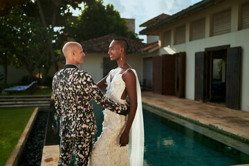 Ambiguous gender fluid black bride in white dress and LGBTQ groom in bold suit marry at tropical...