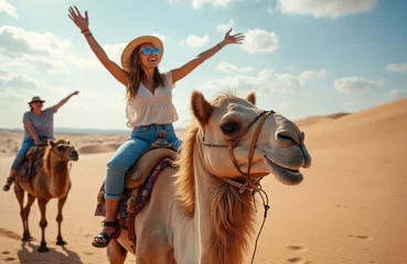 Selbstklebende Fototapeten Happy woman tourists enjoy camel ride tour in Morocco desert. Group of female holidaymakers fun on camels in sunny day. Excited, cheerful. Outdoor adventure in North Africa. Cultural exploration © Maryna