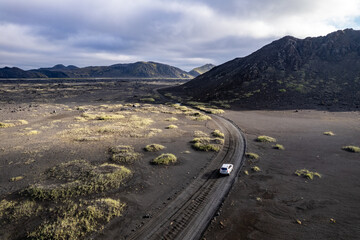 Aerial perspective of a car navigating a sparse basalt road Landmannalaugar in Iceland, surrounded by barren landscapes and bathed in warm sunlight