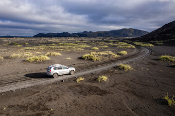 Aerial perspective of a car navigating a sparse basalt road Landmannalaugar in Iceland, surrounded by barren landscapes and bathed in warm sunlight