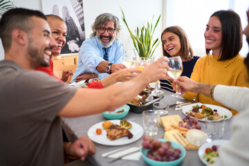 Caucasian family of different generations laughing toasting with white wine at meal at table...