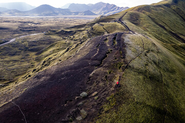 Stunning aerial image showcasing a woman walking over volcanic crater surrounded Landmannalaugar mountains and by hills and expansive wilderness, emphasizing the raw beauty and geology of volcanic