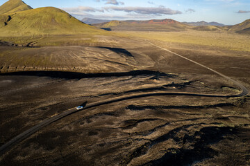 Aerial perspective of a car navigating a sparse basalt road Landmannalaugar in Iceland, surrounded by barren landscapes and bathed in warm sunlight