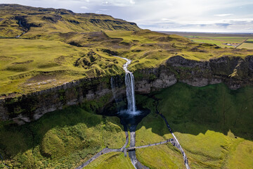 A magnificent aerial view Seljalandsfoss waterfall in Iceland plunges over the edge of green cliffs, surrounded by stunning countryside. The serene landscape captures beauty of untouched nature
