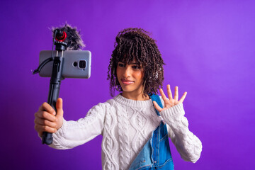 Young latin influencer recording content with smartphone and external microphone on purple...