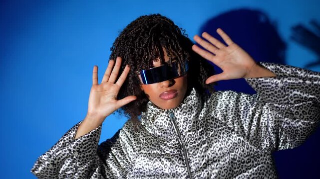 Young woman wearing futuristic visor interacting with virtual reality, making gestures on blue background