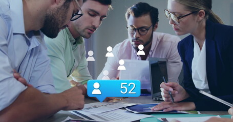 Image of social media icons with number over diverse colleagues having meeting in office