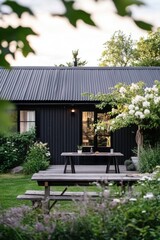 Fototapeta premium Nestled within a lush garden filled with vibrant blooming flowers, this enchanting black cottage exudes charm, especially as the sun sets, casting a beautiful glow