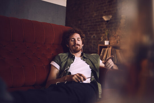 Man relaxing on couch with headphones and a smartphone in bar