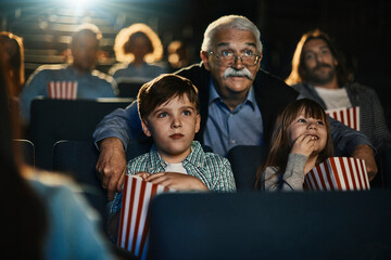 Grandfather with grandchildren watching movie in cinema with popcorn