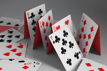 Collapsed house of playing cards on grey background, closeup