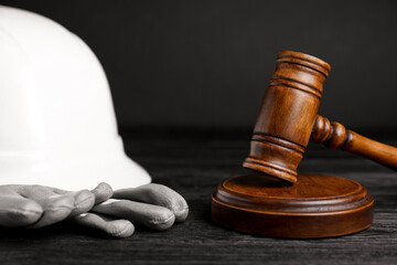 Accident at work concept. Gavel and construction worker's protective gear on black wooden table