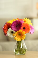 Bouquet of beautiful gerbera flowers in glass vase on wooden table indoors