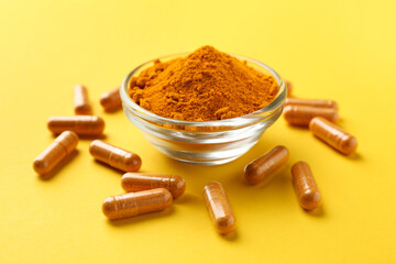 Turmeric powder in bowl and capsules on yellow background, closeup