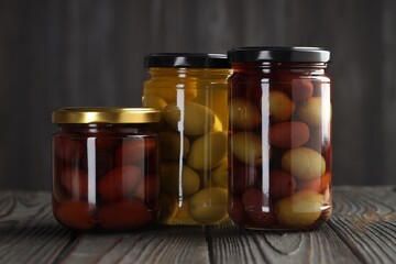 Pickled olives in glass jars on wooden table against gray background