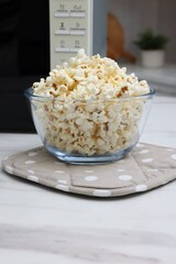 Tasty popcorn in bowl near microwave oven on white marble table indoors