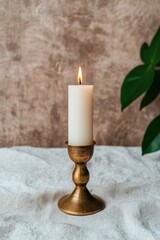 A lit candle in a gold candle holder on a linen tablecloth.