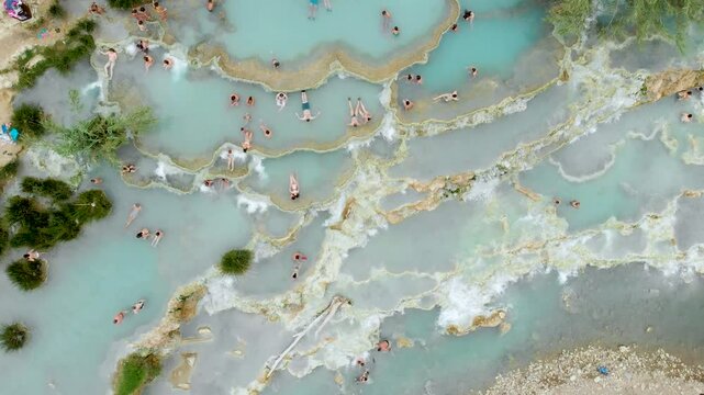 Aerial summer top-down view of Terme di Saturnia, geothermal sulfur springs and natural spa with waterfalls at Saturnia thermal baths. People bathing at Cascate del Mulino, Grosseto, Tuscany, Italy.