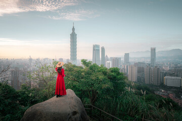 Fototapeta premium Beautiful asian woman in red dress and hat standing on the peak of Hong Kong city at sunset 