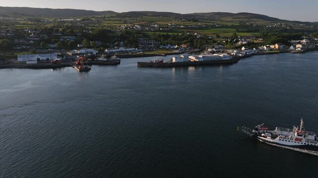 Lough Foyle Ferry, County Donegal, Ireland, June 2023. Drone pulls backwards tracking left as it orbits to frame a transport vessel approaching the Greencastle Harbour in the soft evening light.