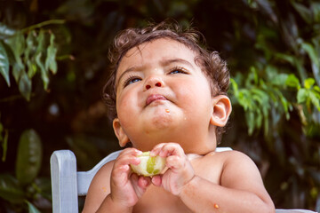 9-month-old baby eating lemon in his white highchair, outdoors.