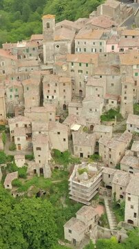 Aerial summer afternoon view of Sorano. Rooftops of an ancient medieval hill town hanging from a tuff stone over the Lente River. Etruscan heritage. Province Grosseto, Tuscany, Italy. Vertical footage