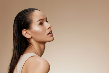 Beautiful young woman with wet hair and natural makeup, showcasing glowing skin and elegance against a soft beige background Perfect for beauty and skincare concepts