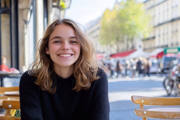 A young woman sitting at a sidewalk cafe with a happy smile, in Paris, warm sunny, day, busy street.