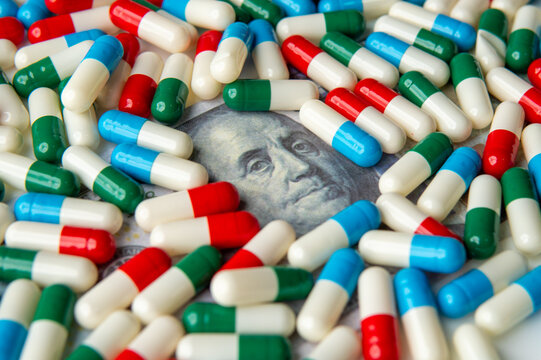 A close-up image of colorful capsules scattered on a US dollar bill. The high cost of medication concept.