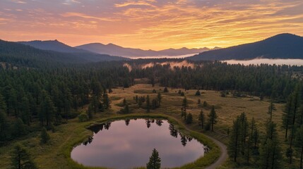 Obraz premium Sunrise over a serene mountain lake, reflecting the colorful sky and surrounded by evergreen trees and a misty valley.
